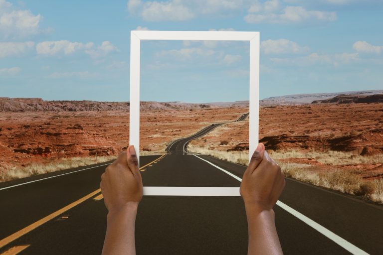 Self-publishing at MindSparkPress: two hands hold an empty white frame over a straight desert road running towards red mesas.